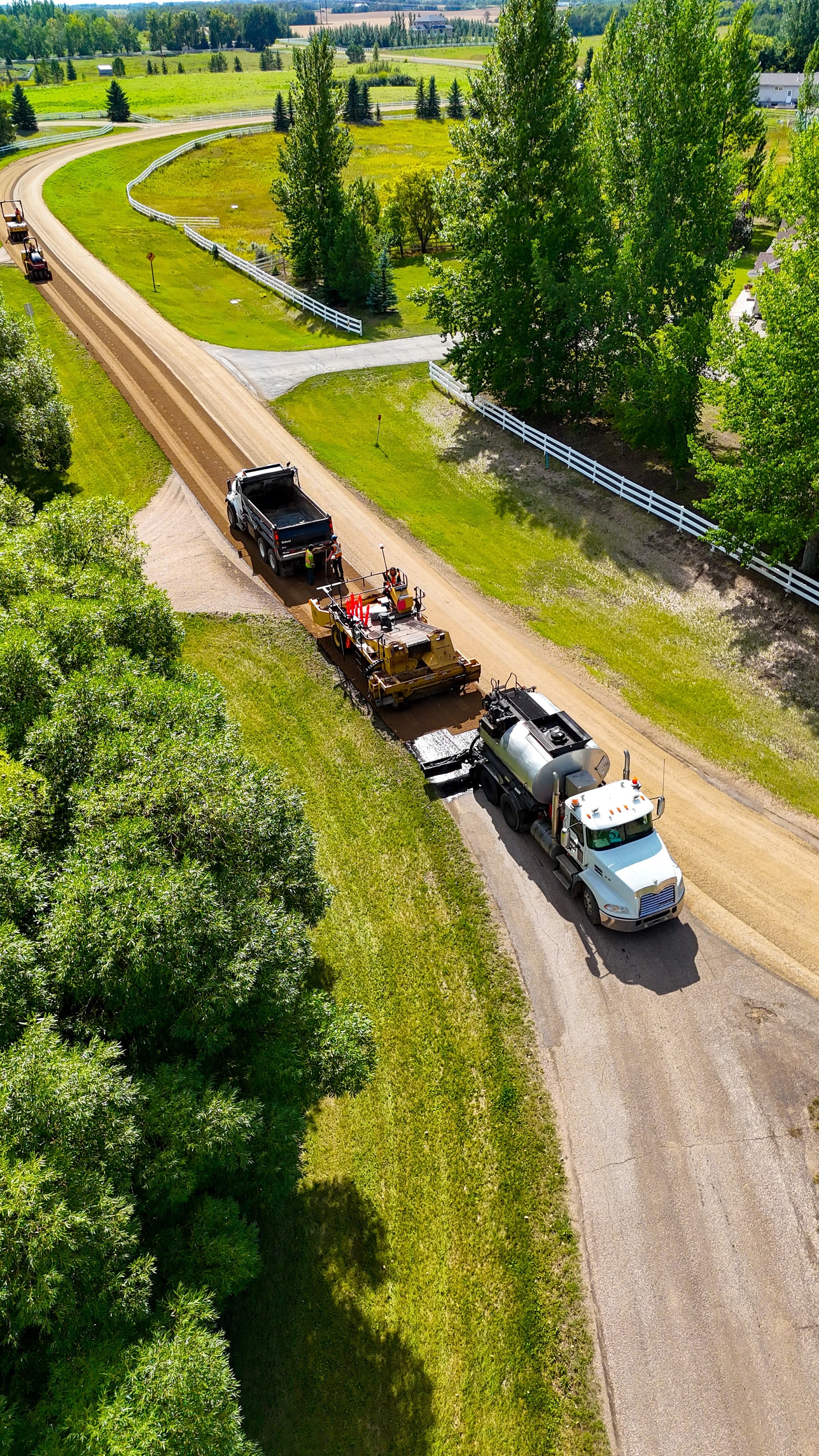 Drone view of a chip spreader and emulsion truck laying a new chip-seal surface on a rural road