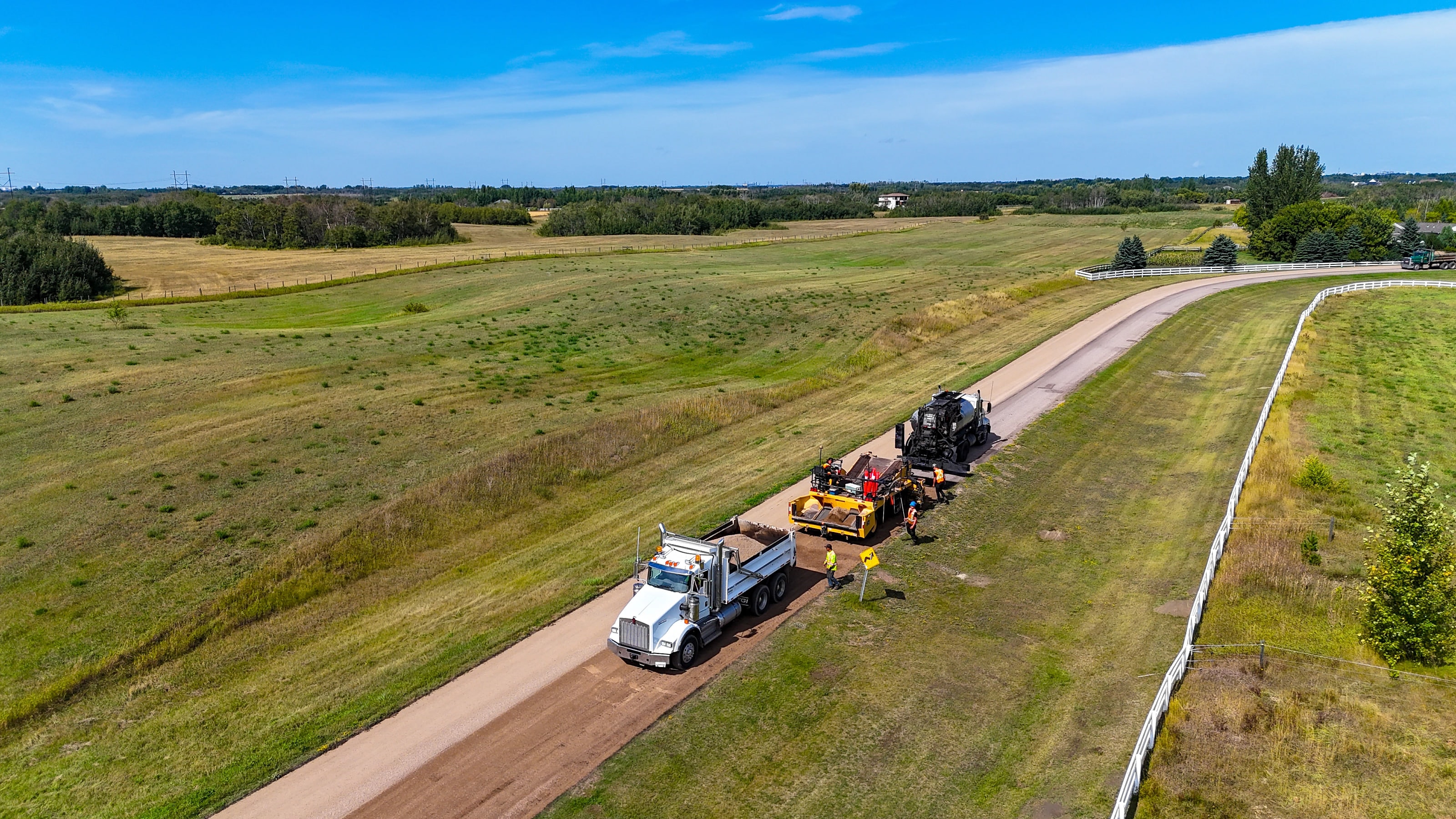 Aerial view of a Raider Asphalt crew treating a rural gravel road across open Saskatchewan prairie