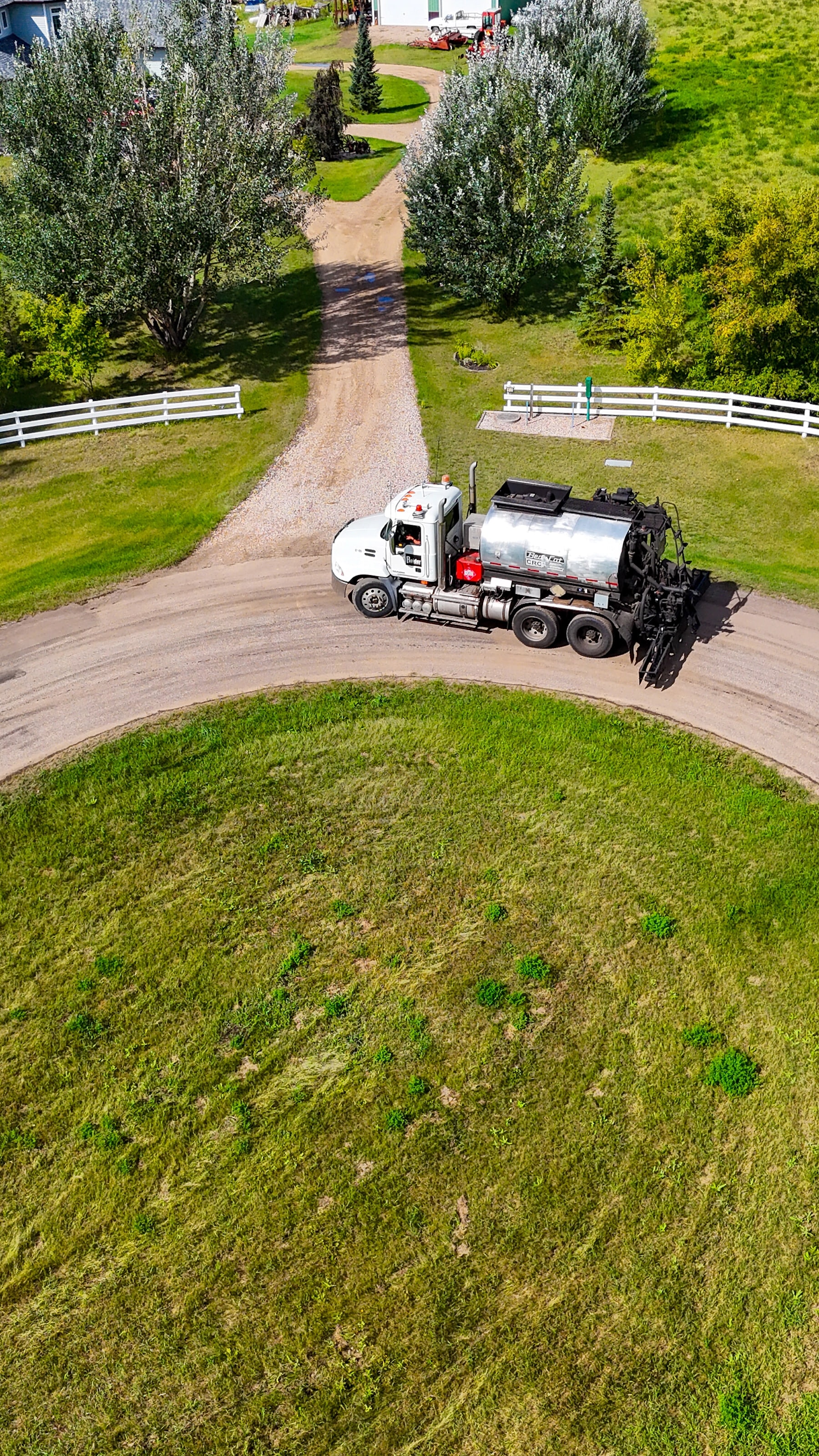 Emulsion spray truck applying dust control on a gravel cul-de-sac, seen from directly above